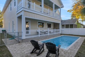 A two-story house with a balcony, a swimming pool, and two Adirondack chairs.
