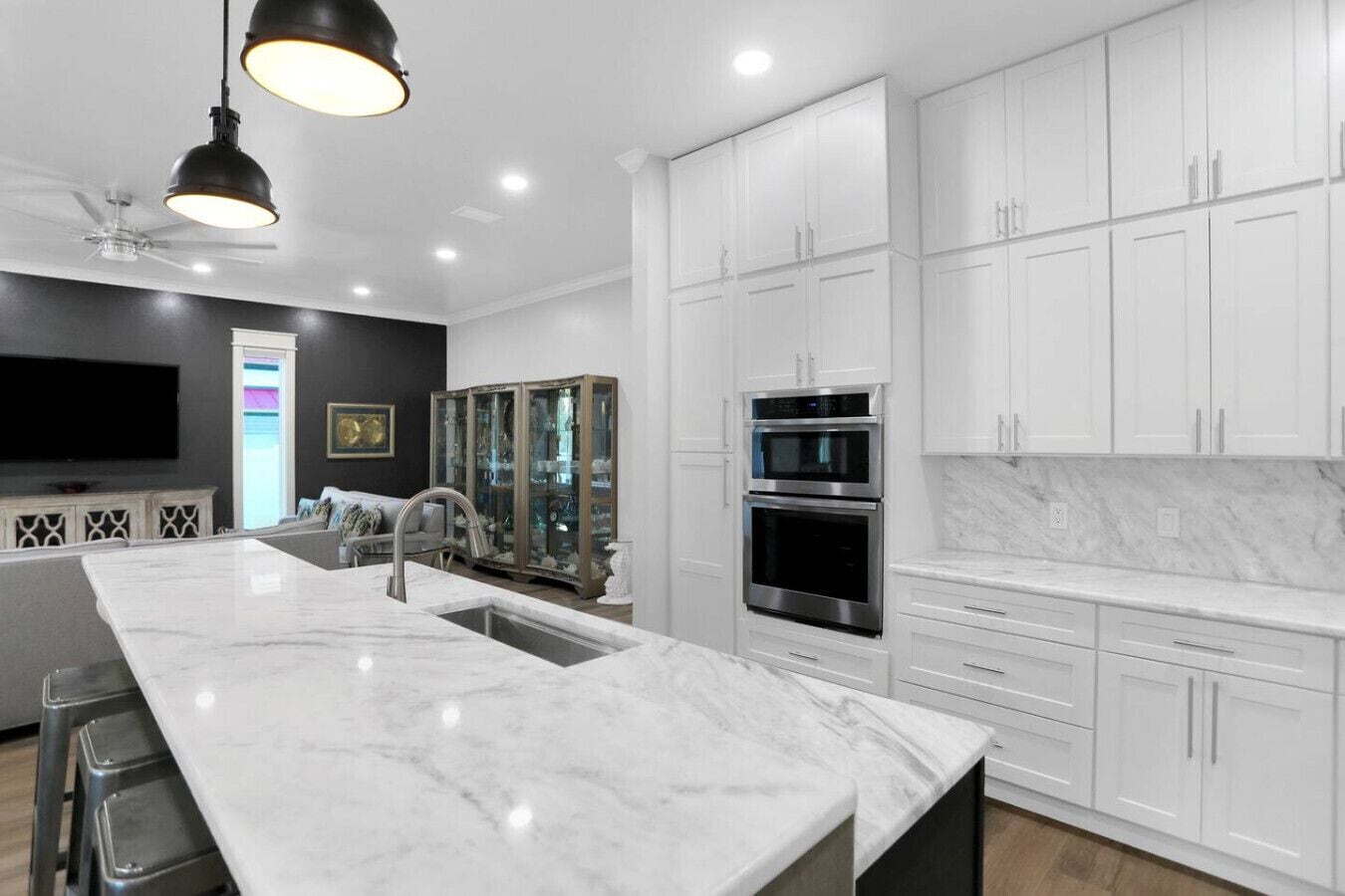 A modern kitchen with white cabinetry, a marble island, stainless steel appliances, and pendant lighting.