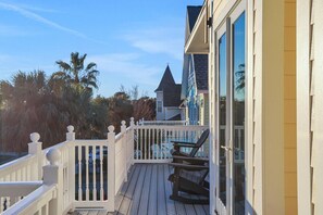 Une terrasse en bois avec une balustrade blanche, une chaise et un bâtiment doté de grandes fenêtres.