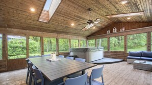 A wooden cabin with a dining table, chairs, a sofa, and a hot tub. - Secluded Retreat w/ Hot Tub, Pickleball/Basketball Court, Putting Green, Arcade (New Buffalo)