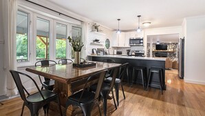A modern kitchen with a central island, large windows, and a dining area with chairs. - Secluded Retreat w/ Hot Tub, Pickleball/Basketball Court, Putting Green, Arcade (New Buffalo)