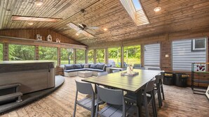 A spacious indoor area with a wooden ceiling, large windows, a seating area with a sofa and chairs, and a dining table. - Secluded Retreat w/ Hot Tub, Pickleball/Basketball Court, Putting Green, Arcade (New Buffalo)