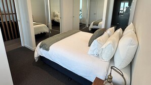 Quarto moderno com uma cama grande, uma mesa de cabeceira com abajur e um espelho.