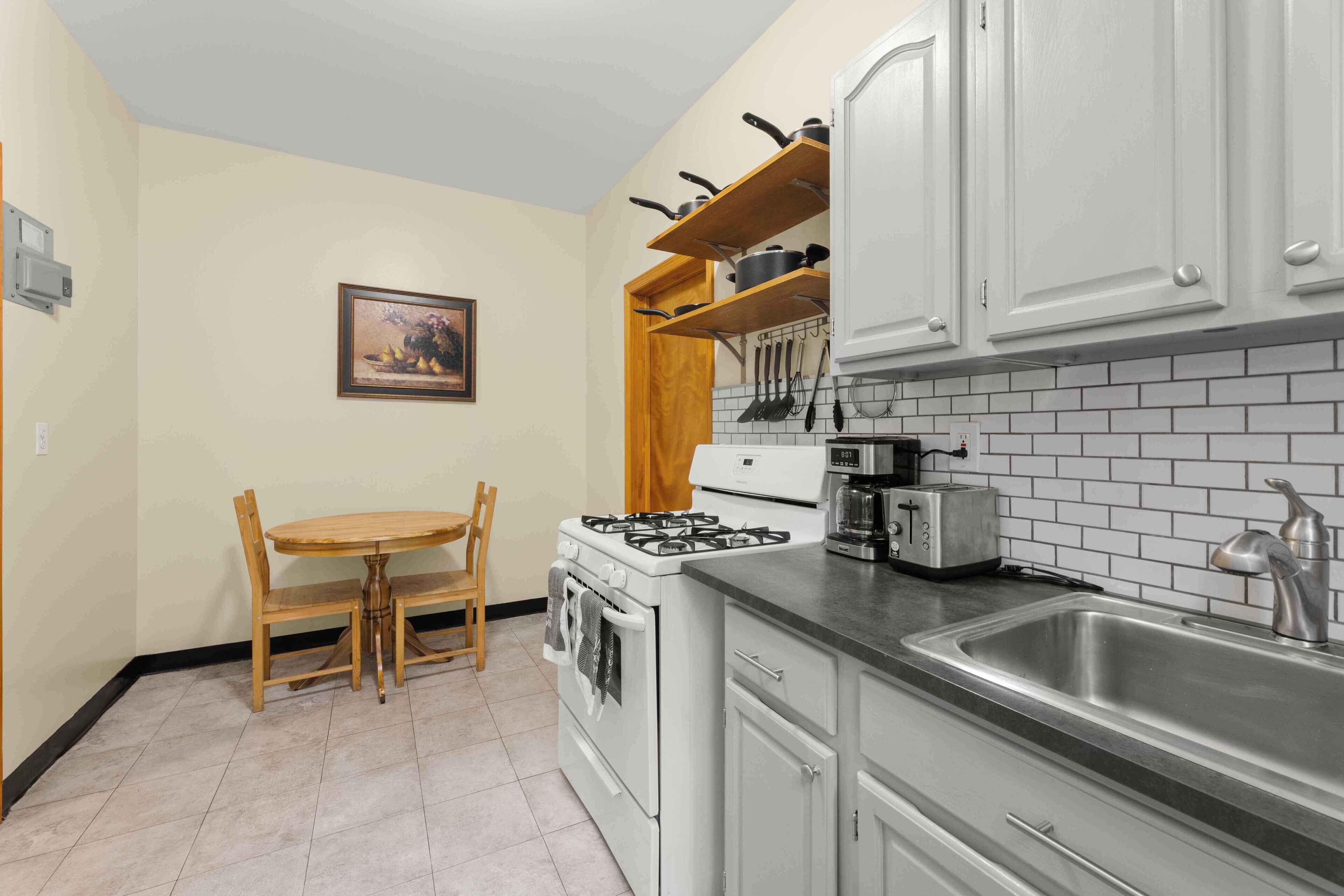 A kitchen with white cabinets, a stove, a sink, and a dining table with chairs.