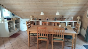 Une table à manger en bois avec des chaises, un réfrigérateur blanc et des suspensions lumineuses dans une cuisine aux murs en bois.