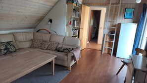 Ein gemĂŒtliches Wohnzimmer mit einer Couch, einem BĂŒcherregal, einer Leiter und einem KĂŒhlschrank.
