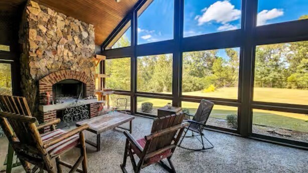 A stone fireplace with a table and chairs in a room with large windows overlooking a green landscape. - 6000 sq ft home with Private Pool and Hot Tub, Sleeps 16 - 13 Acres (Upatoi)