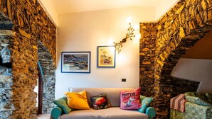 Une pièce chaleureuse avec un mur en pierre, un canapé de couleur turquoise et un tableau encadré représentant un port.