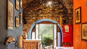 Une pièce avec un mur en pierre, un réfrigérateur rouge, une table recouverte d’une nappe et une porte donnant sur un espace extérieur.