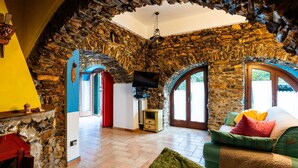 Un intérieur rustique avec des murs en pierre, une cheminée, un téléviseur et un coin salon confortable.