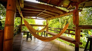 Eine Hängematte unter einer Holzw pergola mit Fliesenboden, umgeben von üppiger Vegetation.