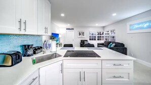 A modern kitchen with white cabinets, a built-in island, and a dining area with a black couch. - Coastal Unit .5 Miles to Beach! (Fort Lauderdale)