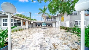 A courtyard with a stone floor, white columns, and a palm tree. - Coastal Unit .5 Miles to Beach! (Fort Lauderdale)