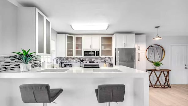 A modern kitchen with white cabinets, a central island with bar stools, a built-in oven, and a refrigerator. - Coastal unit! .5 miles to Beach! (Fort Lauderdale)