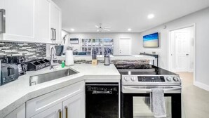 A modern kitchen with white cabinetry, a black stove, a dishwasher, and a coffee station. - Coastal Unit! .5 miles to Beach! (Fort Lauderdale)