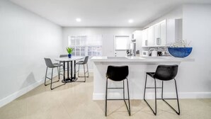 A modern kitchen with white cabinets, a central island, and black bar stools. - Coastal Unit! .5 miles to Beach! (Fort Lauderdale)