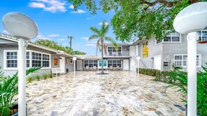 A spacious courtyard with a tiled floor, surrounded by buildings with large windows and a central seating area. - Coastal Unit! .5 miles to Beach! (Fort Lauderdale)