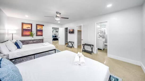 A modern hotel room with a large bed, a desk, and a ceiling fan. There are two doors leading to other rooms and a bathroom. - Coastal Unit! .5 miles to Beach! (Fort Lauderdale)