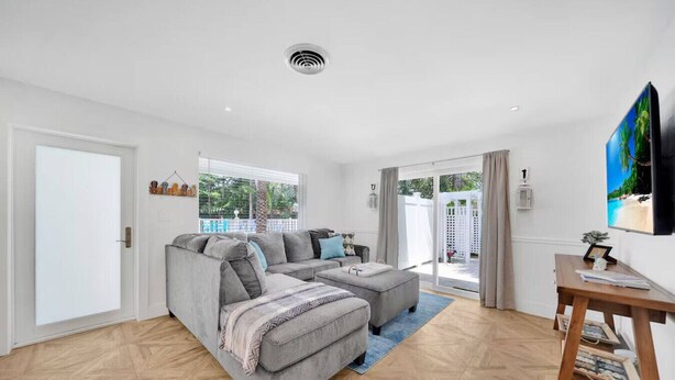 A modern living room with a grey sofa set, a wooden coffee table, and a TV on the wall. - Tropical Paradise+ Pool & Patio! (Fort Lauderdale)