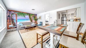 A modern living room with a view of the beach, a dining area with a wooden table, and a kitchen with white cabinets. - Tropical Paradise + Pool & PATIO (Fort Lauderdale)