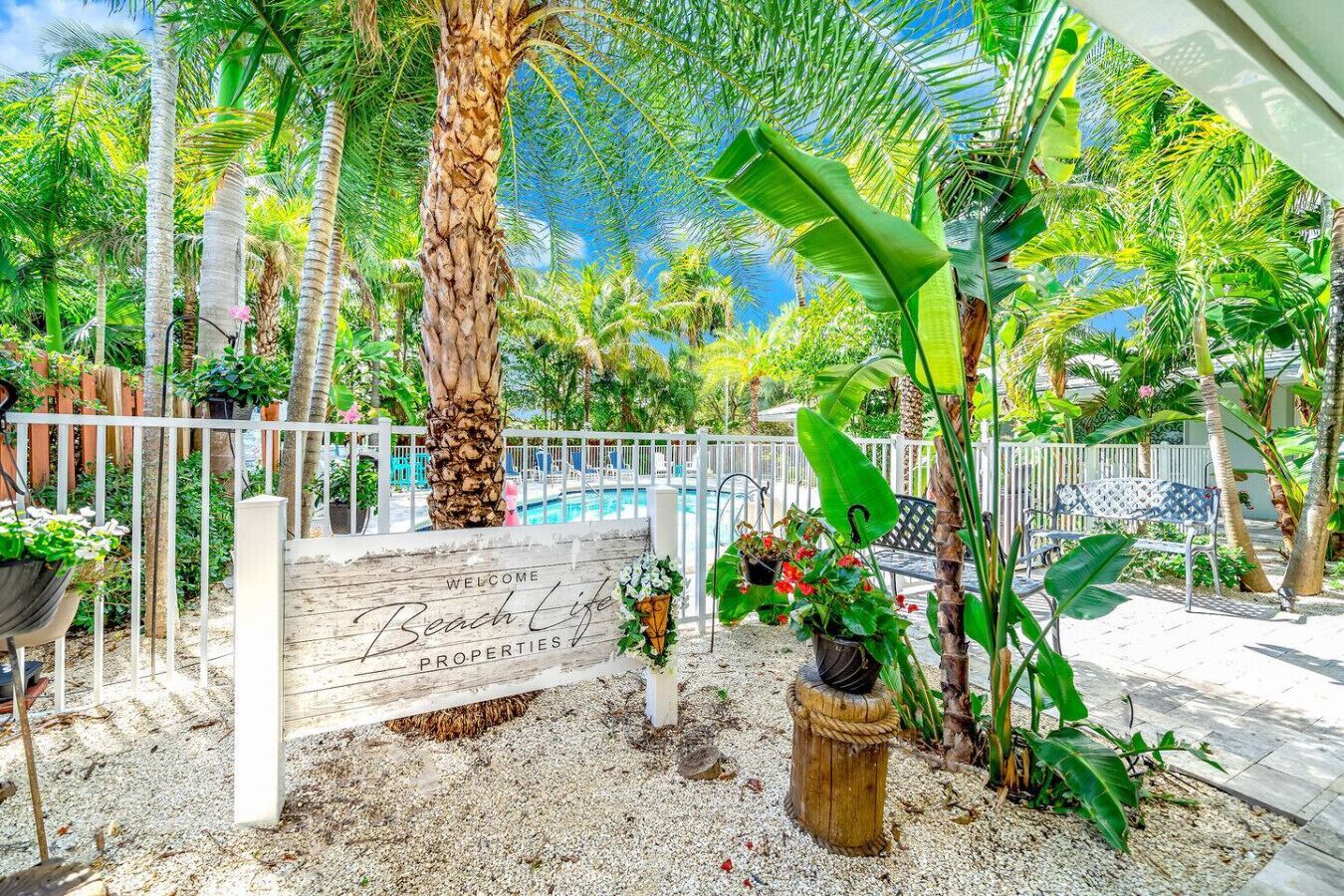 A tropical garden with a wooden sign reading "Welcome Beach Life Properties."