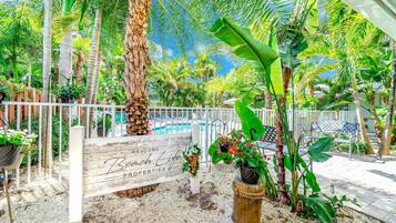 A tropical garden with a wooden sign reading "Welcome Beach Life Properties."