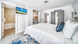 A modern hotel room with a large bed, a walk-in closet, a bathroom with a shower, and a TV displaying a beach scene. - Tropical Paradise + Pool & PATIO (Fort Lauderdale)