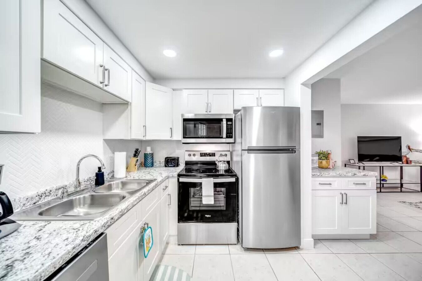 A modern kitchen with white cabinets, stainless steel appliances, a granite countertop, and a built-in oven.