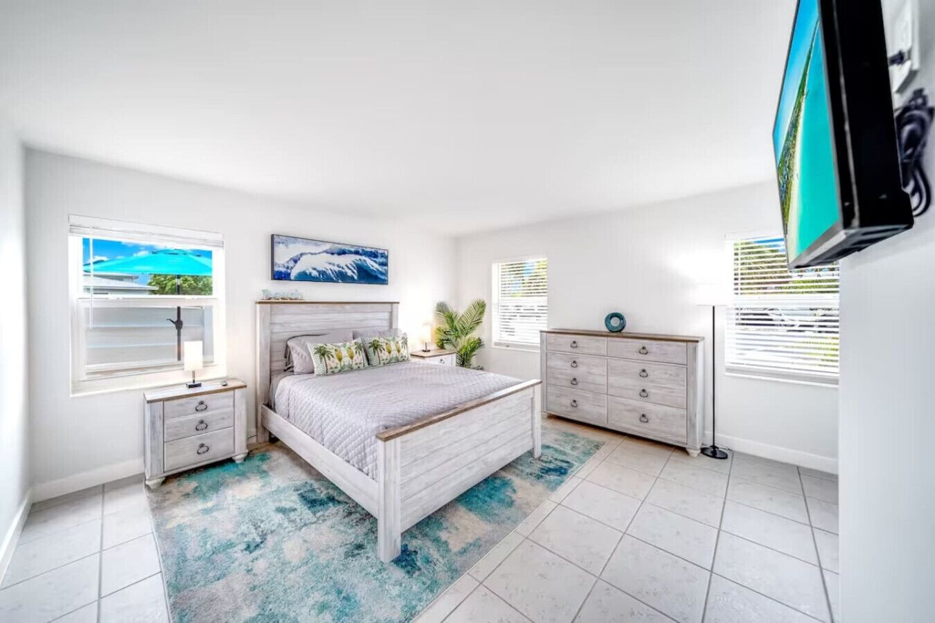 A bedroom with a bed, a dresser, a nightstand, a window with blinds, and a painting on the wall.
