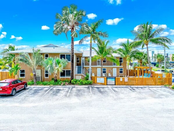 A multi-story hotel with a parking lot, palm trees, and a red car parked in front.