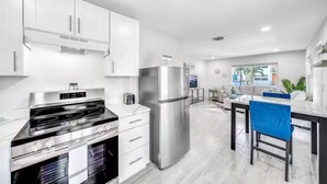 Una cocina moderna con armarios blancos, electrodomésticos de acero inoxidable y una zona de comedor con una silla azul.