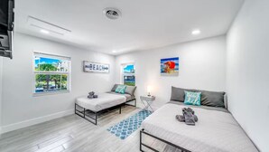 Un dormitorio moderno con dos camas, una ventana con vista a la playa y un cuadro decorativo con motivos playeros.