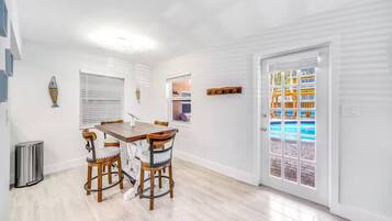 A dining area with a wooden table and chairs, a trash can, and a door leading to a pool area.
