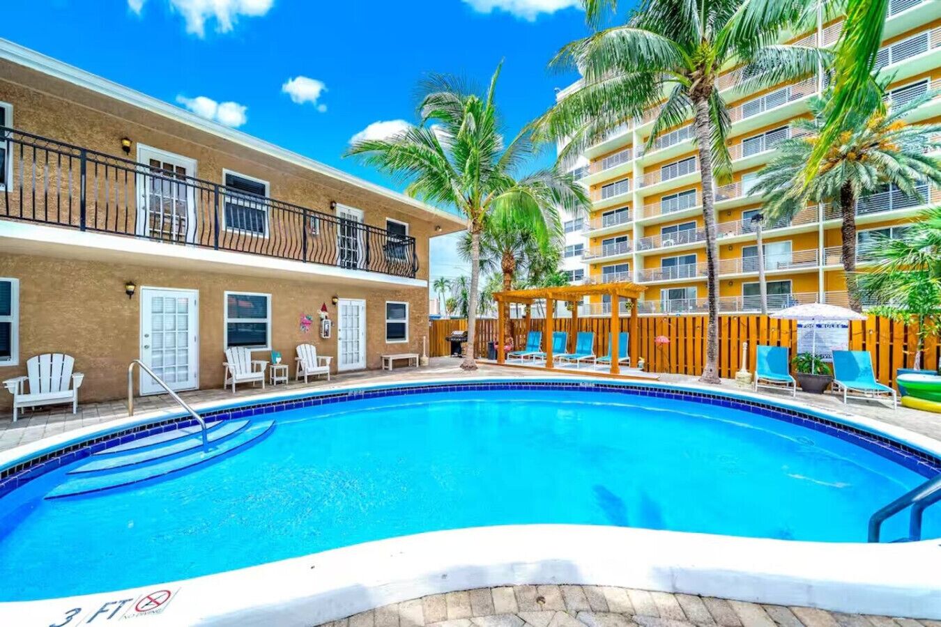 A swimming pool surrounded by palm trees and a multi-story building with balconies.