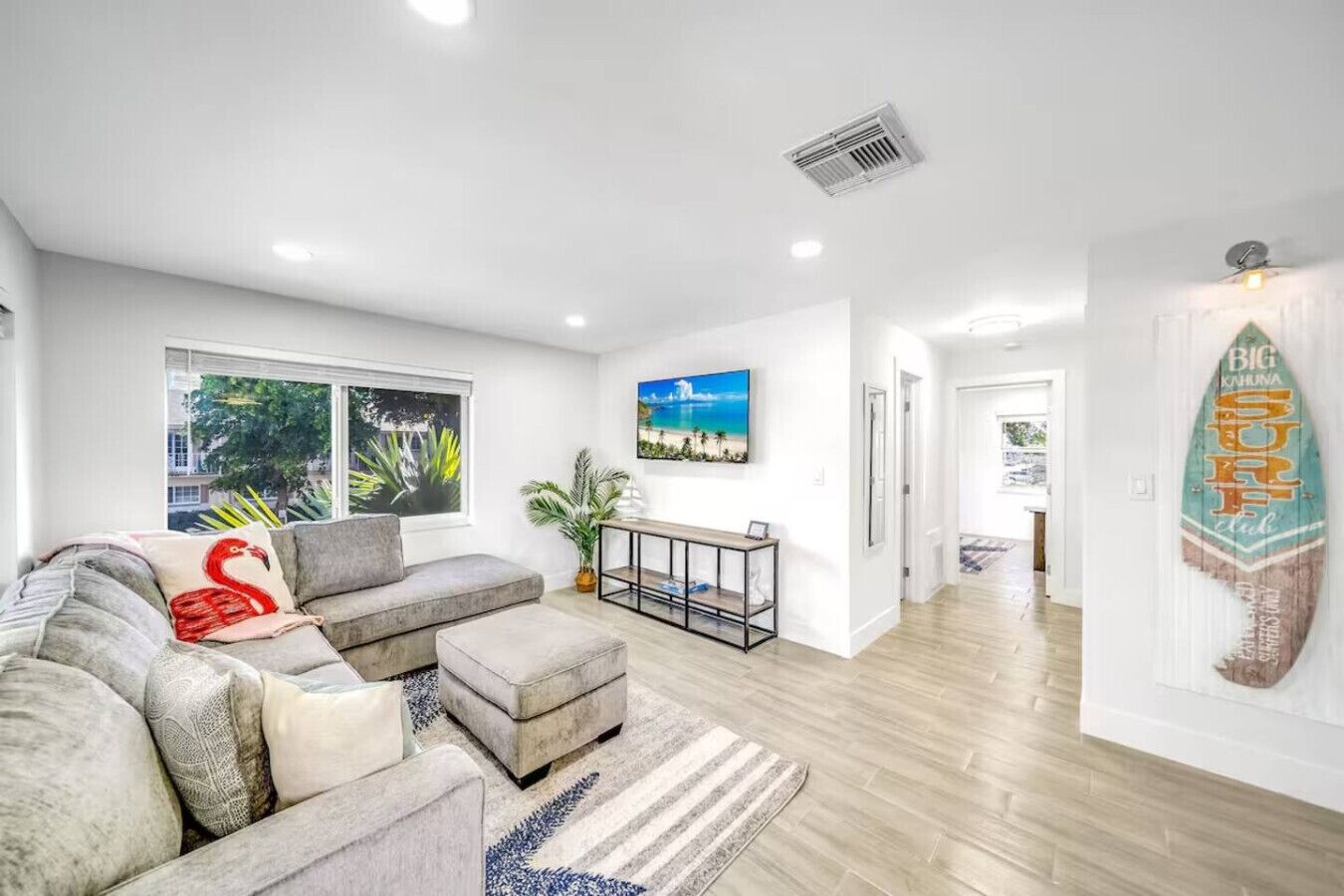 A modern living room with a grey sectional sofa, a small side table, and a large window with a view of greenery.