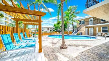 A pool area with lounge chairs, a wooden pergola, and a palm tree.