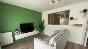 A living room with a green wall, a flat-screen TV, a sofa, and a window with a view. - Bienvenue Chez Annabelle - Meaux (Meaux)