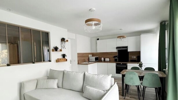 A modern living room with a sofa, dining table, and chairs. There is a kitchen area in the background with cabinets and appliances. - Bienvenue Chez Annabelle - Meaux (Meaux)