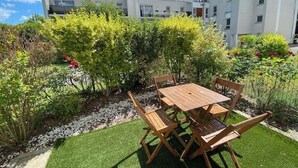 A patio with a wooden table and chairs, surrounded by greenery and a building in the background. - Bienvenue Chez Annabelle - Meaux (Meaux)