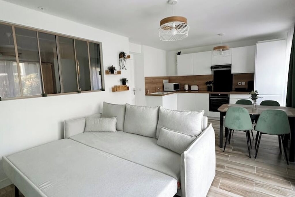 Una sala de estar moderna con un sofá, un comedor con mesa y sillas, y una cocina con armarios y electrodomésticos.