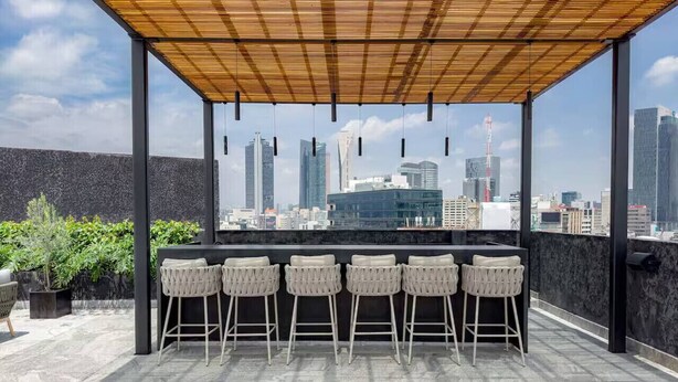 Eine Dachterrasse mit Blick auf die Stadt, mit einer Holzw pergola, sechs Barhocker und einer schwarzen Arbeitsplatte.