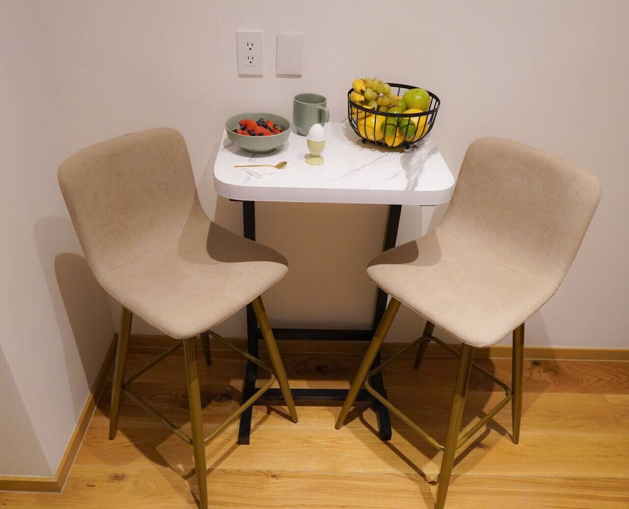 A small dining area with two chairs and a table, a bowl of fruit, a mug, and a spoon.