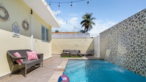 Un patio trasero con piscina, un porche con mobiliario exterior y un muro decorativo.