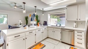 A modern kitchen with white cabinetry, a central island, pendant lighting, and a view to the outside.