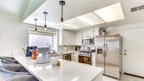 A modern kitchen with white cabinetry, stainless steel appliances, and a central island with bar stools.
