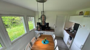 Ett modernt kök med ett matbord i trä, vita skåp och utsikt över grönområden utanför.