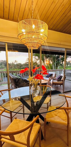 A covered outdoor seating area with wicker chairs, a glass table, and a hanging chandelier.