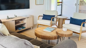 Ein modernes Wohnzimmer mit Flachbildfernseher, Holzmöbeln und einem großen Fenster mit Jalousien.