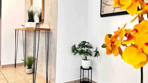 A hallway with a tiled floor, a mirror on the wall, a small table with a potted plant, and a framed picture of yellow flowers. - La Casa de Ada Near Airport & Beaches Charming 3-bedroom house with AC andWiFi (San Juan)