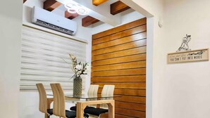 A dining area with a wooden table and chairs, a vase with flowers, and a wall with a wooden panel and a framed quote. - La Casa de Ada Near Airport & Beaches Charming 3-bedroom house with AC andWiFi (San Juan)